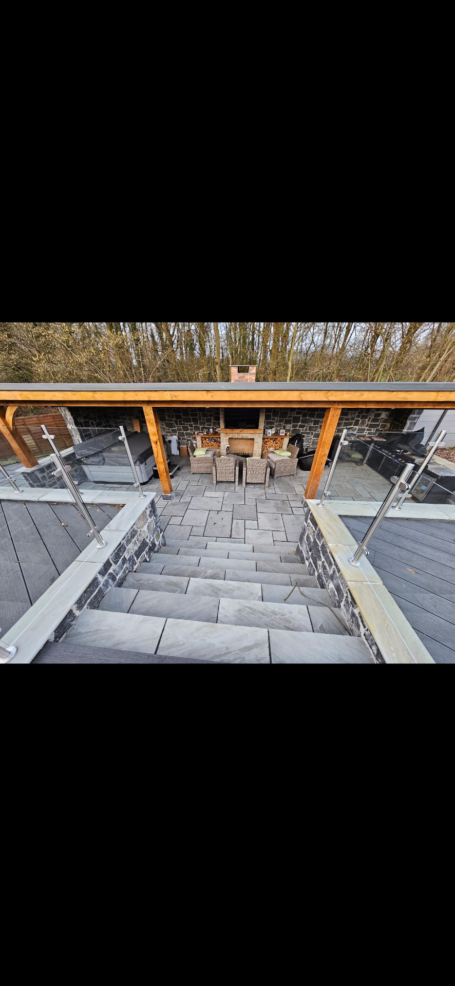 Outdoor stone terrace with a timber pergola, fireplace and seating area